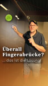 Ein Mann mit Mütze und Brille, der mit einem Tuch die Oberfläche eines dunklen Schranks reinigt, dazu der deutsche Text: Überall Fingerabdrücke? … das ist die Lösung!.