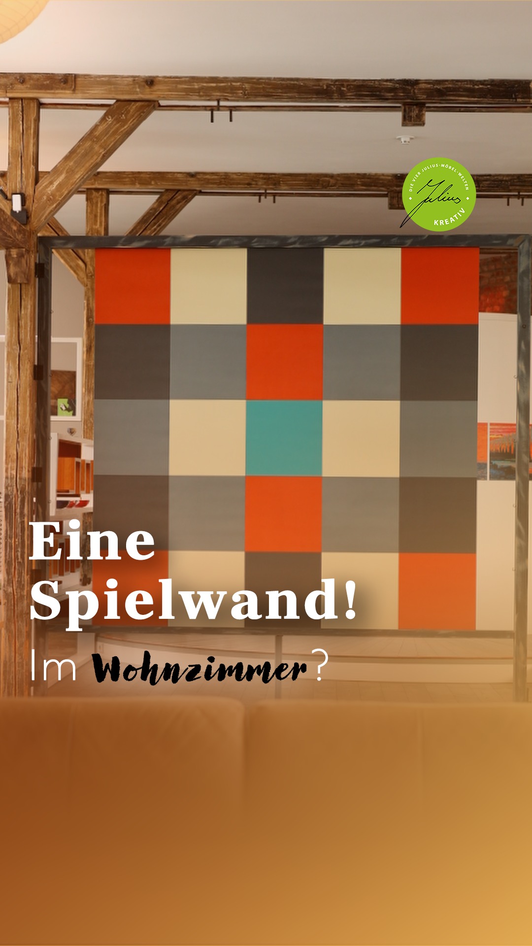 Eine bunte, karierte Spielwand trennt ein gemütliches Wohnzimmer mit Holzbalken. Der deutsche Text lautet: „Eine Spielwand! Im Wohnzimmer?“ In der rechten oberen Ecke befindet sich ein grünes, rundes Etikett.