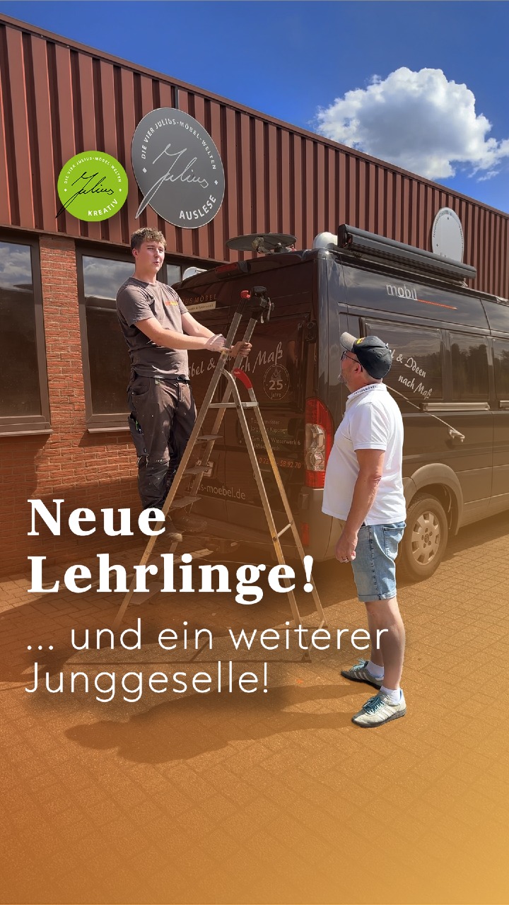 Vor einem Industriegebäude stehen zwei Männer neben einem schwarzen Transporter; einer arbeitet auf einer Leiter, der andere steht neben ihm. Der deutsche Text lautet: „Neue Lehrlinge! … und ein weiterer Junggeselle!“.