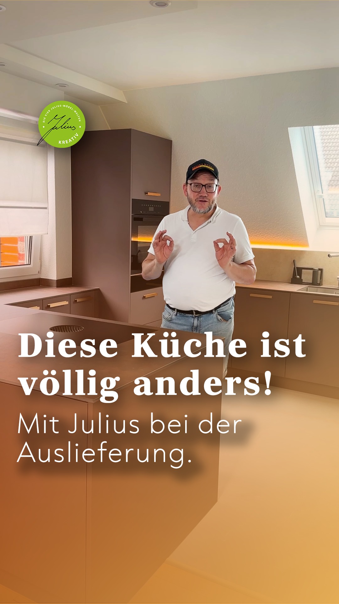 Ein Mann steht in einer modernen Küche und macht mit beiden Händen eine „OK“-Geste. Der deutsche Text lautet: „Diese Küche ist völlig anders! Mit Julius bei der Auslieferung…“.