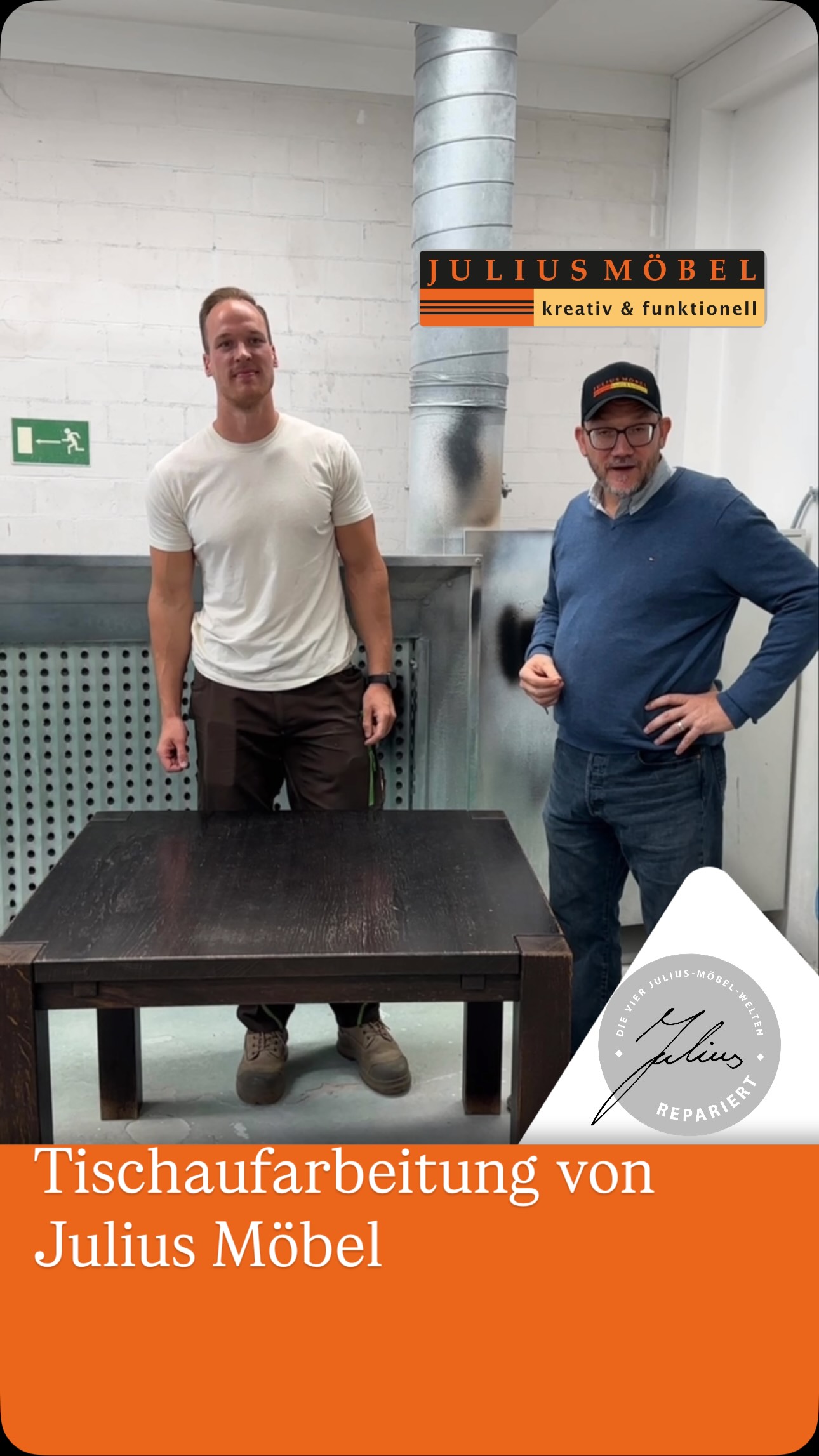 Zwei Männer stehen in einer Werkstatt neben einem dunklen Holztisch. Hinter ihnen befindet sich ein silbernes Lüftungsrohr. Auf einem Logo steht „Julius Möbel“. Unten ist der Text „Tischaufarbeitung von Julius Möbel“ zu lesen.