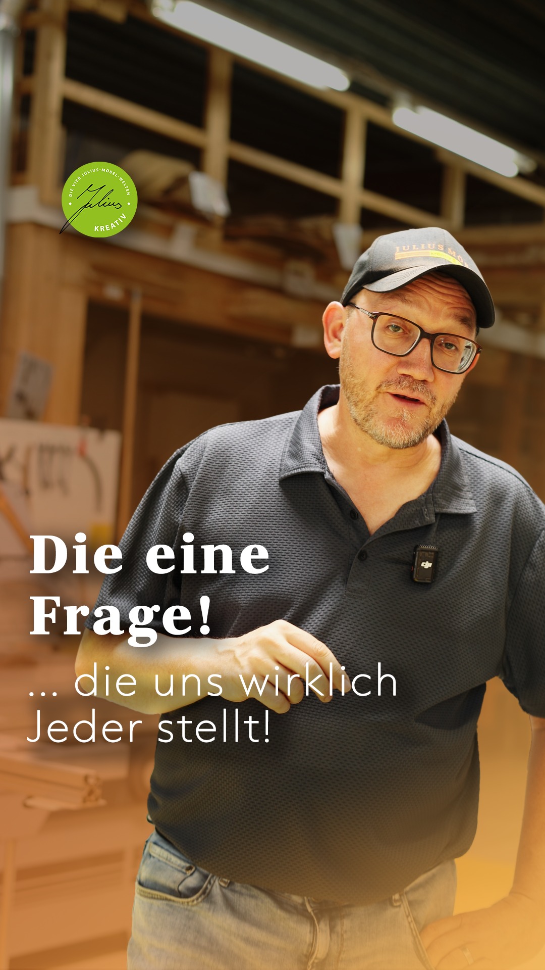 Ein Mann mit Brille, schwarzer Mütze und dunklem Hemd steht in einer Werkstatt und gestikuliert mit einer Hand. Der deutsche Text lautet: „Die eine Frage! … die uns wirklich jeder stellt!“.