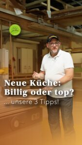 Ein Mann in einem weißen Polohemd und einer Mütze steht in einer Küchenwerkstatt. Der deutsche Text auf dem Bild lautet: Neue Küche: Billig oder top? … unsere 3 Tipps! Im Hintergrund sind Holzbalken und Küchenelemente zu sehen.