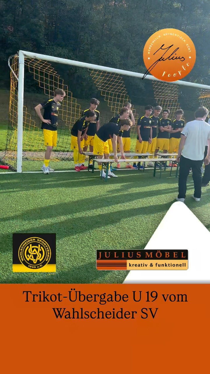 Eine Jugendfußballmannschaft in gelb-schwarzen Trikots versammelt sich auf einem sonnigen Spielfeld vor einem Tor und nimmt neue Trikots entgegen, die ein Mann an sie verteilt. Am unteren Bildrand sind Sponsorenlogos und Schriftzüge zu sehen.