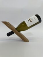Der Weinflaschenhalter „Balance“ hält eine Weinflasche horizontal am Flaschenhals in einem Holzständer mit einem einzigen diagonalen Schlitz und sorgt so vor einem schlichten weißen Hintergrund für eine der Schwerkraft trotzende Optik.
