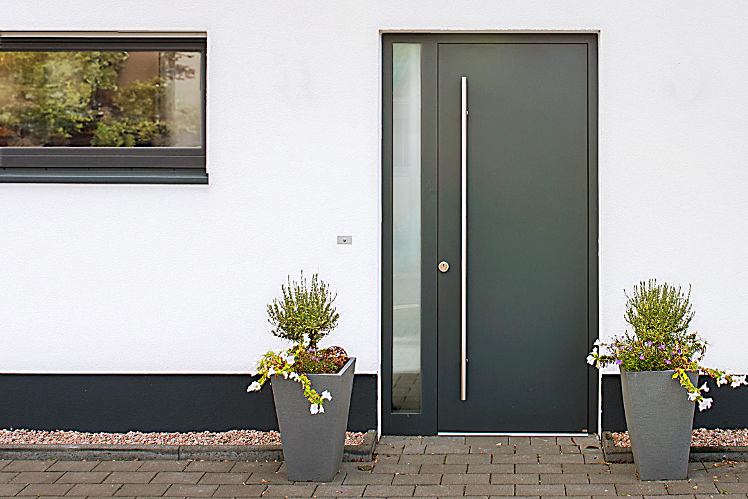 Holz-Alu-Haustür nach Maß: anthrazitfarbene Haustür mit langem Griffstab an einer weißen Fassade