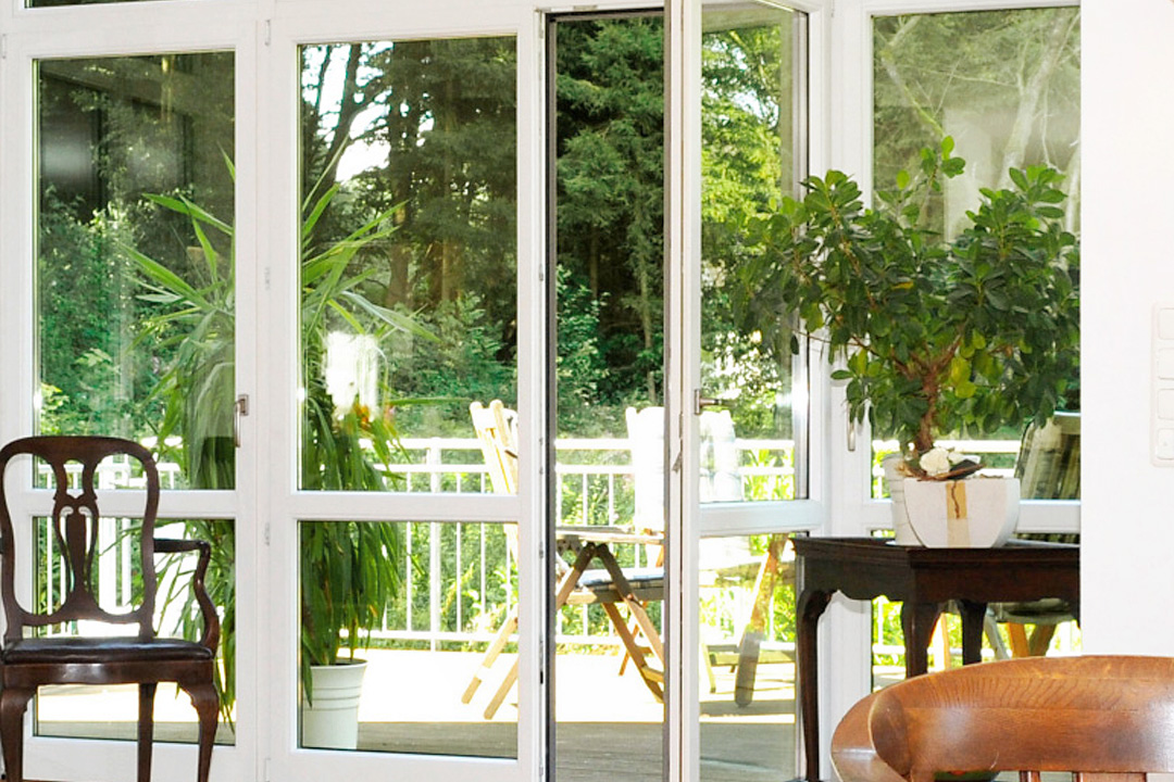 Kunststofffenster nach Maß: weiße Fenstertüren mit Blick auf eine Terrasse im Grünen